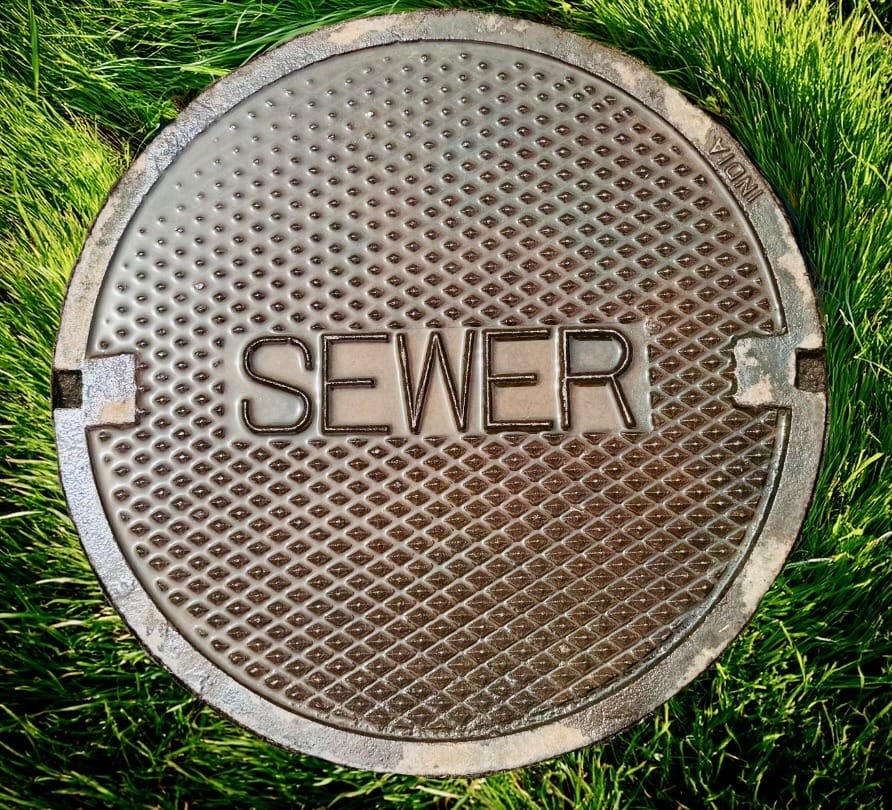 metal septic cover with the words sewer with green grass around it