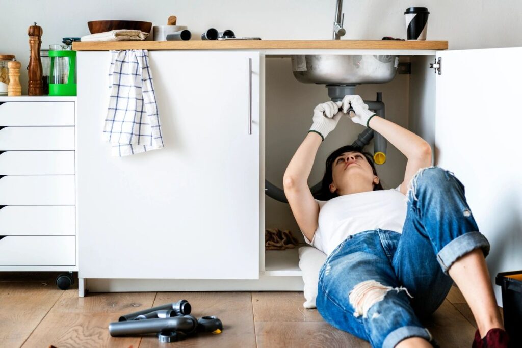 women under kitchen sink opening clogged drain pipe