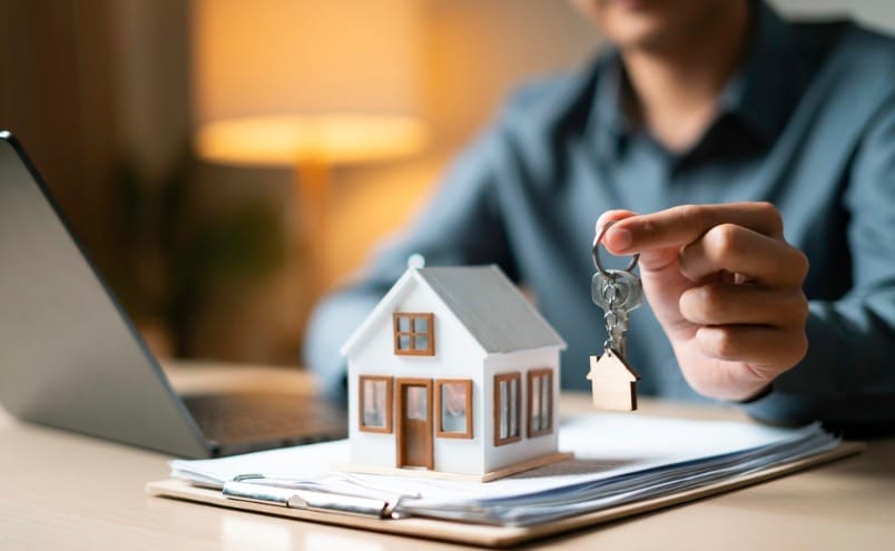 home model on top of paper work with a person holding a key